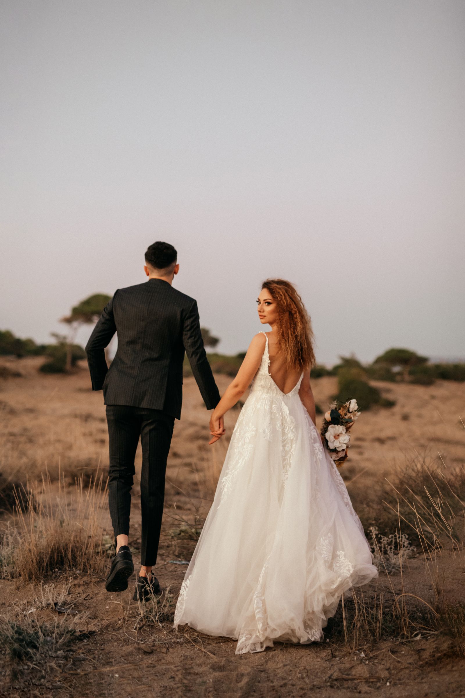 Bride and groom walking hand in hand through the desert at sunset